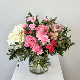 Pink roses, carnations, and white hydrangeas arranged in a clear glass vase