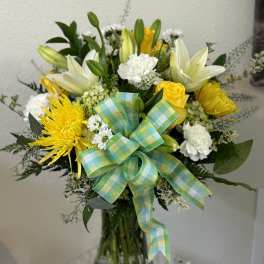 Yellow and white flower bouquet in a glass vase with a plaid ribbon