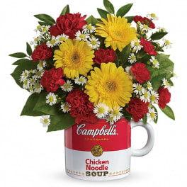 Yellow gerbera daisies, red carnations, and small white daisies in a Campbell's soup mug.