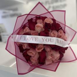 Bouquet of pink and red roses wrapped in pink paper with a ribbon
