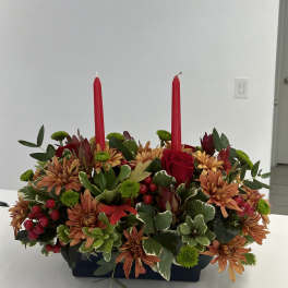 Red candles in a low floral centerpiece with orange blooms and greenery