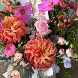 Mixed bouquet with large orange dahlias and pink blooms in a white vase