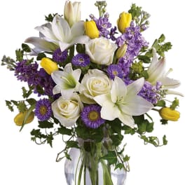 Bouquet of white lilies, roses, and purple flowers in a glass vase