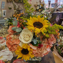 Bouquet with sunflowers, white roses, and peach hydrangeas in a glass vase