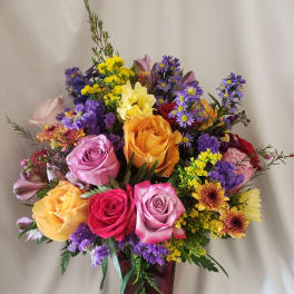 Mixed bouquet of roses and purple filler flowers in a burgundy vase