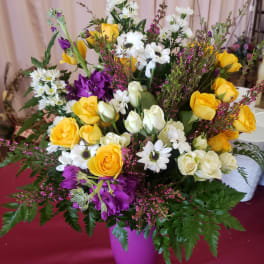 Mixed bouquet of yellow roses, white daisies, and purple flowers in a vase