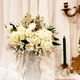 White floral arrangement in a tall vase beside a green candle