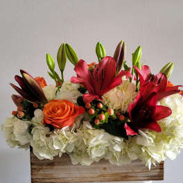 Arrangement of red lilies, orange roses, and white hydrangeas in a wooden box