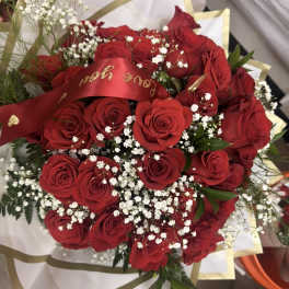 Bouquet of red roses and white filler flowers wrapped in white and gold paper with a red love message ribbon.