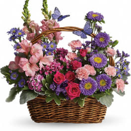 Mixed pink and purple flowers in a wicker basket with butterfly picks