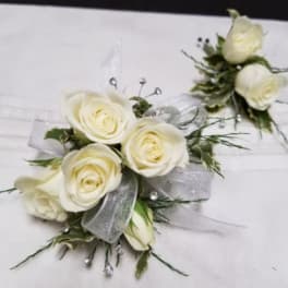 White rose corsages with silver ribbon and greenery