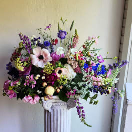 Large mixed bouquet in a white pedestal vase with pink, purple, and blue flowers