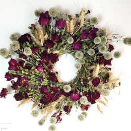 Circular wreath of burgundy flowers and pale seed heads on a white background
