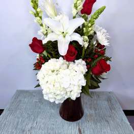 Red roses and white lilies arranged in a vase with white hydrangeas