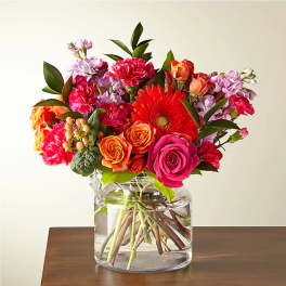 Bright bouquet of pink roses, orange roses, gerbera daisy and carnations in a round glass vase