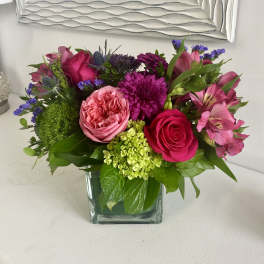 Pink and purple mixed flower arrangement in a square glass vase