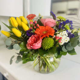 Mixed bouquet with yellow tulips, pink roses, and orange gerbera daisies in a glass vase