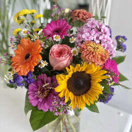 Bright mixed bouquet with sunflower, gerbera daisies, and a rose in a clear glass vase
