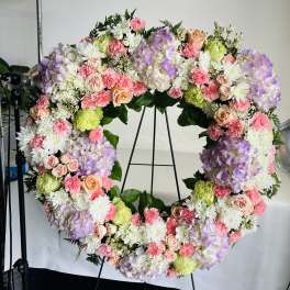 Large pastel floral wreath on a stand with roses, hydrangeas, and carnations