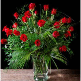 Red roses arranged in a clear glass vase with lush greenery