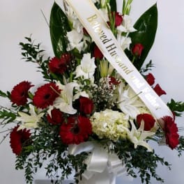 Tall red and white floral arrangement in a white vase with a ribbon sash