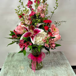 Pink and white mixed flower arrangement in a glass vase with a pink ribbon