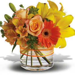 Bouquet of yellow lilies, orange roses, and a gerbera daisy in a glass vase