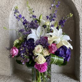 Bouquet of white lilies, purple flowers, and pink roses in a glass vase