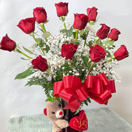 Red roses in a vase with a teddy bear and heart decoration
