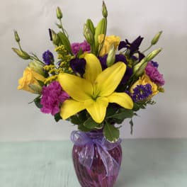 Bouquet of yellow lilies, purple flowers, and pink carnations in a purple vase