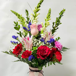 Mixed bouquet of red, pink, and white flowers in a pink vase