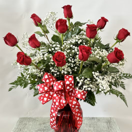 Red roses in a glass vase with a heart-patterned ribbon