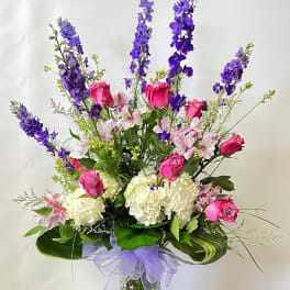Tall bouquet of pink roses, white hydrangeas, and purple delphinium in a glass vase