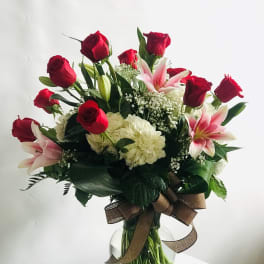 Red roses and pink lilies in a glass vase with a brown ribbon