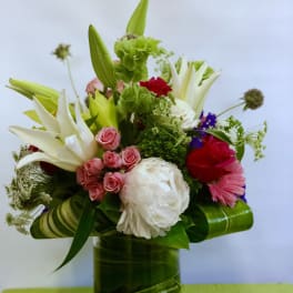 Mixed bouquet in a green glass vase with lilies, roses, and a white peony