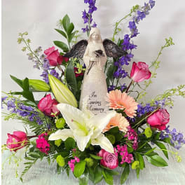Sympathy floral arrangement with angel figurine, lilies, roses, and purple blooms