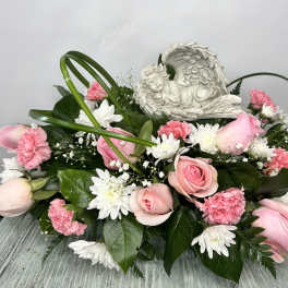 Pink roses and white daisies arranged around a sleeping angel figurine