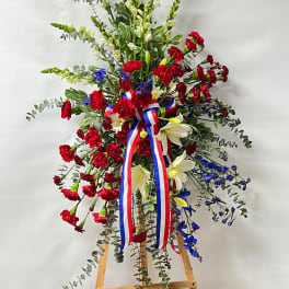 Tall floral standing spray with red, white, and blue flowers on an easel