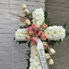 White floral standing cross with pink roses and a "Rest In Peace" ribbon
