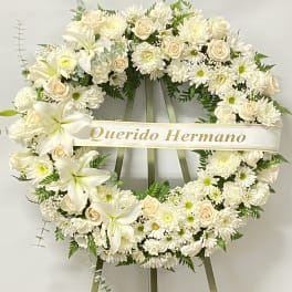 White floral funeral wreath on an easel with a ribbon reading "Querido Hermano"
