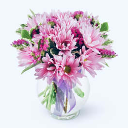 Pink daisy bouquet in a clear glass vase with a purple ribbon