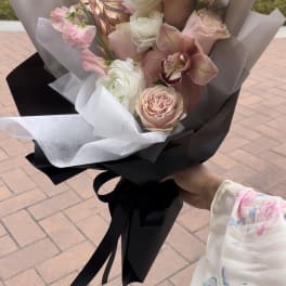 Hand-tied bouquet of pink roses, white ranunculus, and an orchid wrapped in black and white paper