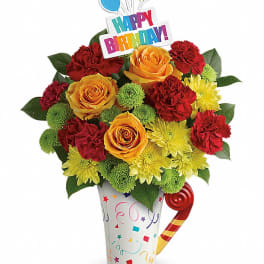 Bright birthday bouquet of red carnations, yellow mums, and orange roses in a confetti mug with a Happy Birthday pick