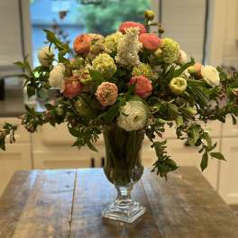 Mixed bouquet of coral, white, and green flowers in a clear glass vase