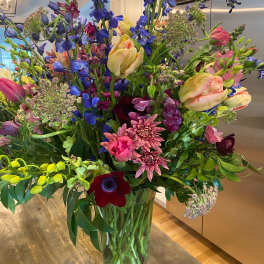 Tall mixed bouquet with blue, pink, yellow, and burgundy flowers in a glass vase