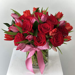 Bouquet of red roses and pink tulips in a glass vase with a pink ribbon