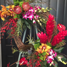 Asymmetrical wreath of red, orange, and pink tropical flowers on a wooden easel.