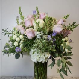 Large bouquet of pale pink roses, white hydrangea, and purple flowers in a glass vase
