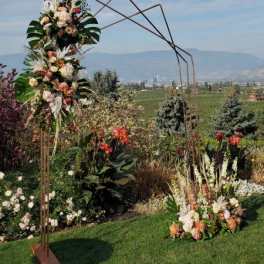 Tall geometric metal arch decorated with peach and white flowers in a garden setting