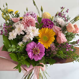 Bright hand-tied bouquet with pink roses, yellow sunflower, and mixed pink and white blooms wrapped in pink paper
